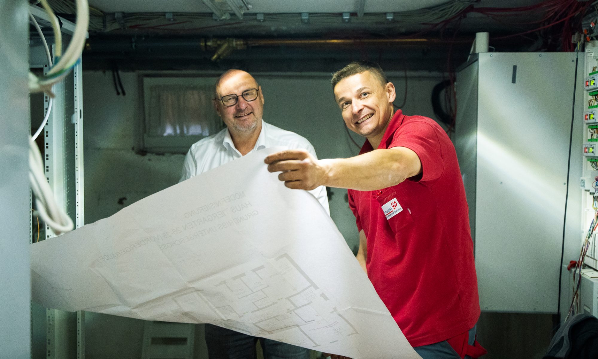 Zwei Kollegen begutachten und besprechen Baupläne in einer Werkstatt oder auf der Baustelle.